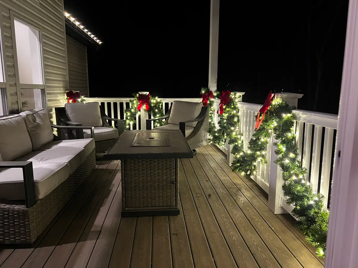 A covered porch with lit garland and deep red bows along the railing
